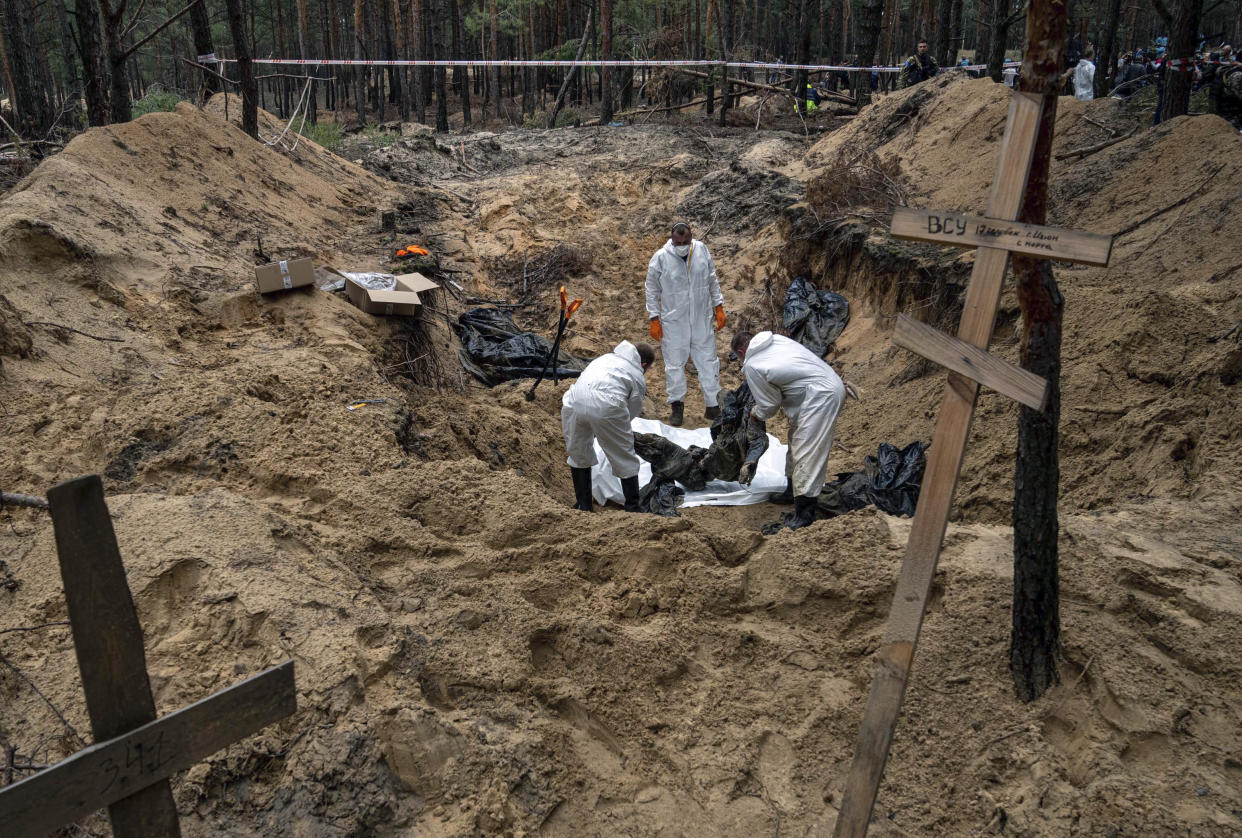Experts lift a body during an exhumation in the recently retaken area of Izium, Ukraine, Friday, Sept. 16, 2022. Ukrainian authorities discovered a mass burial site near the recaptured city of Izium that contained hundreds of graves. It was not clear who was buried in many of the plots or how all of them died, though witnesses and a Ukrainian investigator said some were shot and others were killed by artillery fire, mines or airstrikes. (AP Photo/Evgeniy Maloletka)
