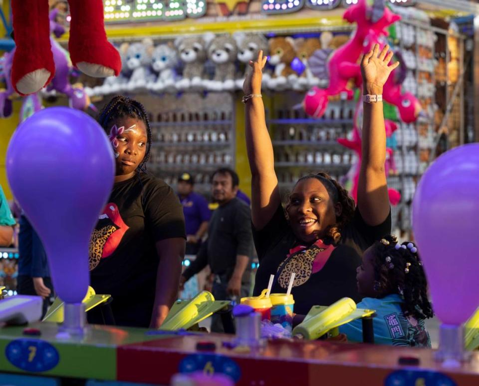 Jewel Evans, center, throws her hands up after winning the Balloon Blast game against Ashanti Evans, left, and Amelia Martin during the Youth Fair opening day on Thursday, March 14, 2024, at the Miami-Dade Fair and Exposition.