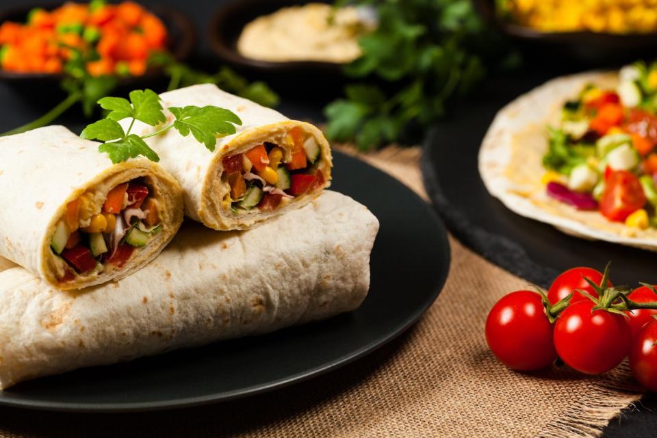 Burritos on a plate, next to tomatoes and other fixings.