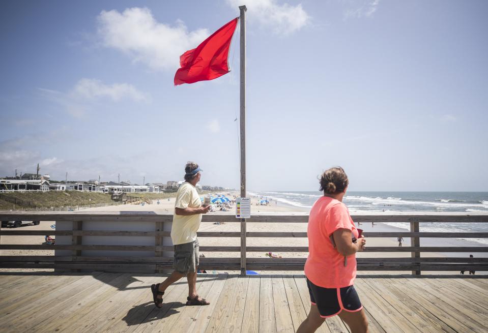 Patrons of the Bogue Inlet Pier in Emerald Isle, N.C. walk past a red flag signaling hazardous swimming conditions as Tropical Storm Isaias approaches the southeast on Sunday, Aug. 2, 2020. (Julia Wall/The News & Observer via AP)