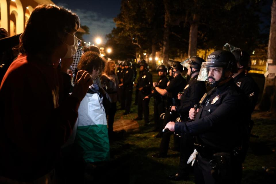 Police officers in riot gear form a line facing student protesters.