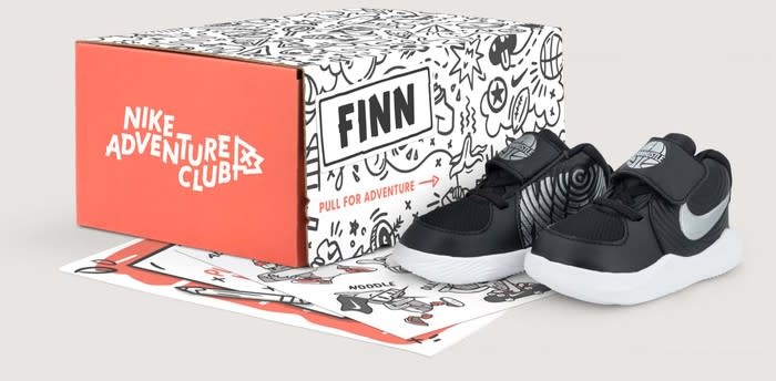 A shoebox with the caption Nike Adventure Club, with a pair of black sneakers sitting next to the box.