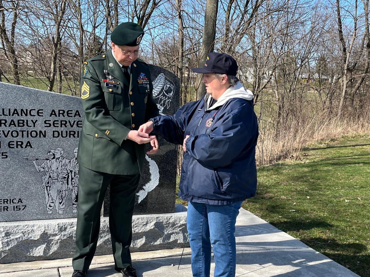 Retired U.S. Army Sgt. 1st Class Sherman Brick receives a challenge coin from Deborah Hughes of Jane Bain Chapter National Society of Daughters of the American Revolution during a ceremony March 29 at the Vietnam Veterans Memorial in Alliance.