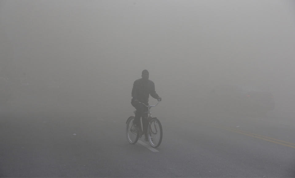 A man rides a bicycle through heavy smoke that is emitting from a nearby store on fire, Monday, April 27, 2015, during unrest following the funeral of Freddie Gray in Baltimore. (AP Photo/Patrick Semansky)