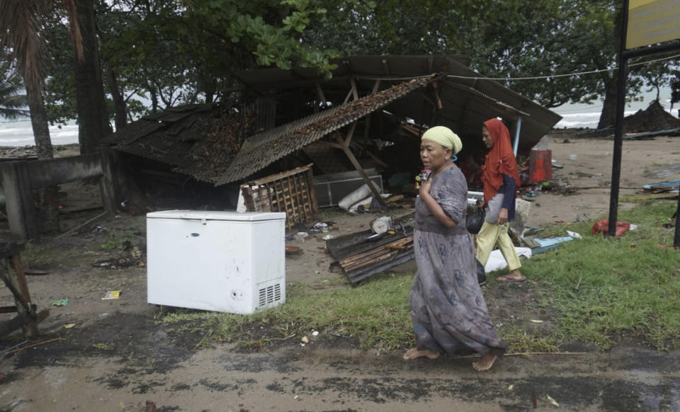 Residents walk past a house damaged by a tsunami, in Carita, Indonesia, Sunday, Dec. 23, 2018. The tsunami apparently caused by the eruption of an island volcano killed a number of people around Indonesia's Sunda Strait, sending a wall of water crashing some 65 feet (20 meters) inland and sweeping away hundreds of houses including hotels, the government and witnesses said. (AP Photo/Dian Triyuli Handoko)