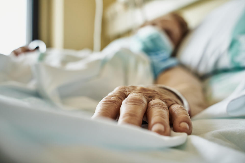 A woman lies in a hospital bed wearing a mask