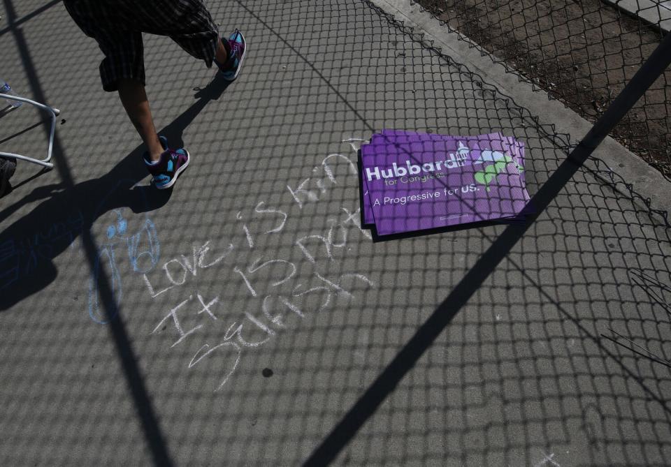 Signs reading, "Hubbard A progressive for US" stacked on a sidewalk that says, "Love is kind It is not selfish" in chalk.