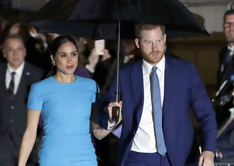 Meghan Markle and Prince Harry walking with an umbrella