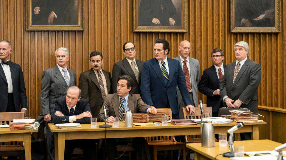 Several of The Plumbers standing around a table in the courtroom in White House Plumbers.