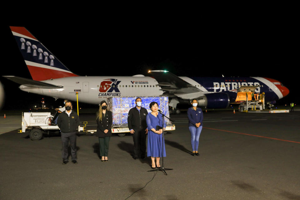 In this photo provided by El Salvador's presidential press office, China's ambassador to El Salvador Ou Jianhong speaks during a ceremony to receive containers of Chinese-made Sinovac COVID-19 vaccines, transported by The New England Patriots team plane, behind, at the airport in San Salvador, El Salvador, late Tuesday, May 18, 2021. (El Salvador's presidential press office via AP)