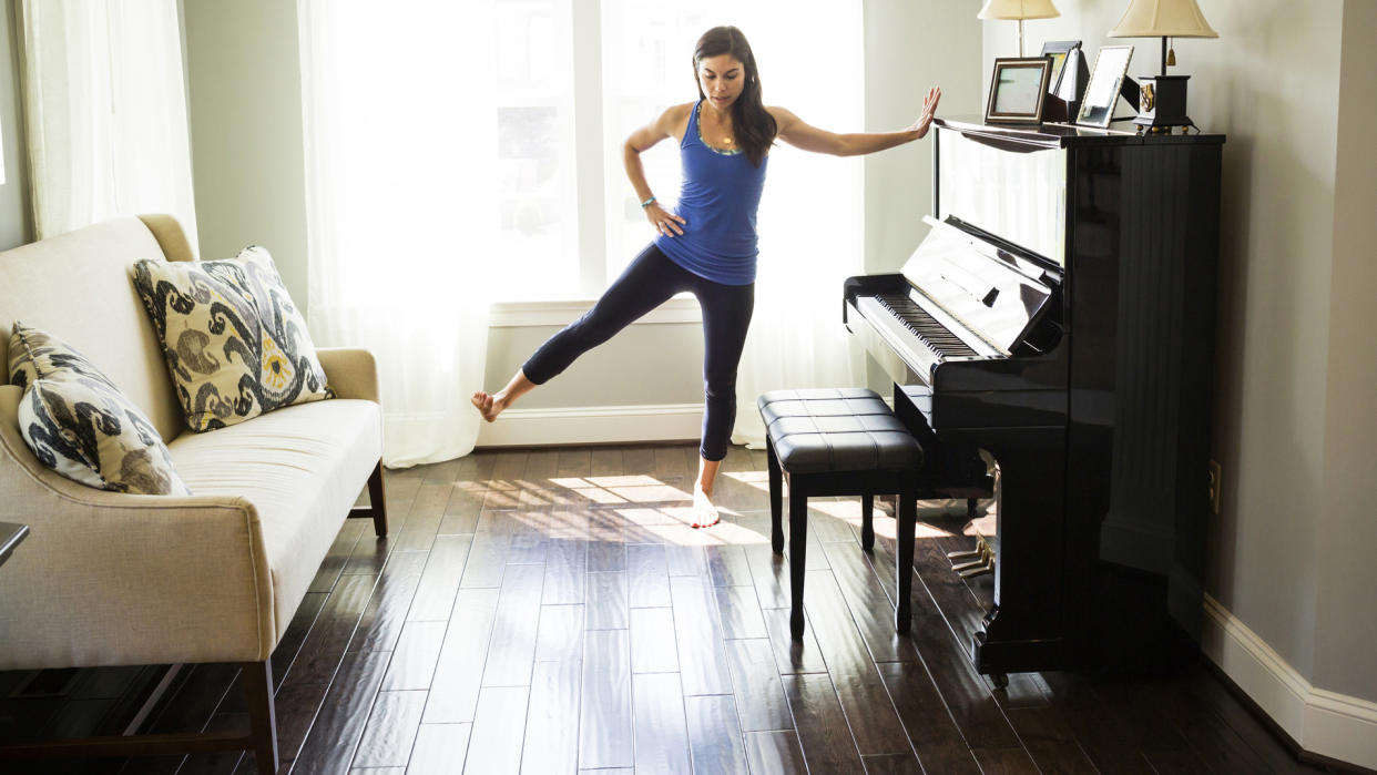  Woman leaning against a piano in front room and stretching out her leg to the side. 