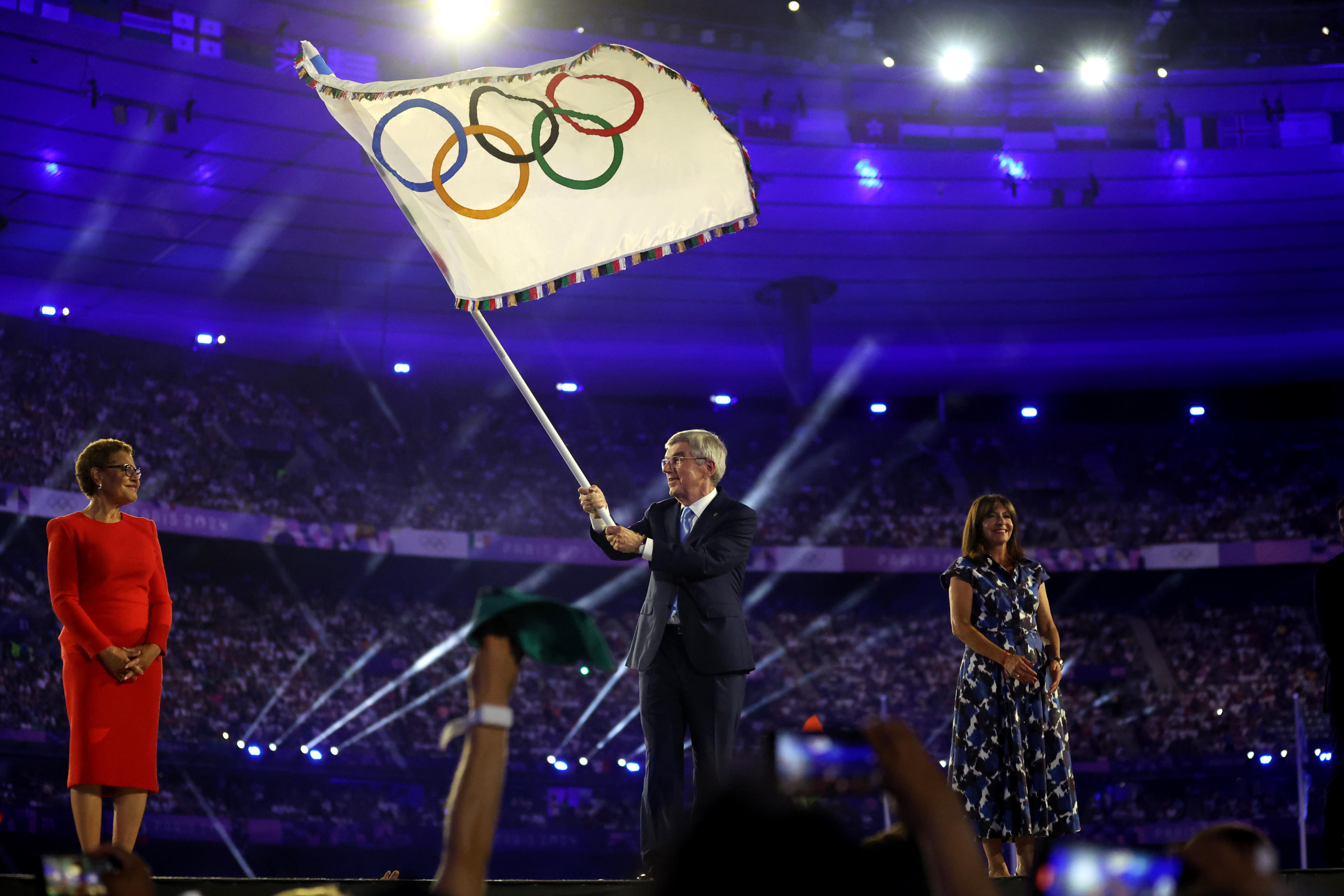 PARIS, FRANCE - AUGUST 11: Thomas Bach, President of International Olympic Committee (C), waves the Olympic Flag as Anne Hidalgo, Mayor of Paris (R), and Karen Bass, Mayor of Los Angeles (L), during the Closing Ceremony of the Olympic Games Paris 2024 at Stade de France on August 11, 2024 in Paris, France. (Photo by Carl Recine/Getty Images)