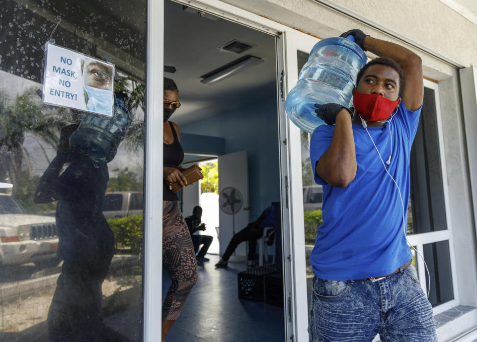 A man carries drinking water for a customer at a water depot store before the arrival of Hurricane Isaias in Freeport, Grand Bahama, Bahamas, Friday, July 31, 2020. (AP Photo/Tim Aylen)