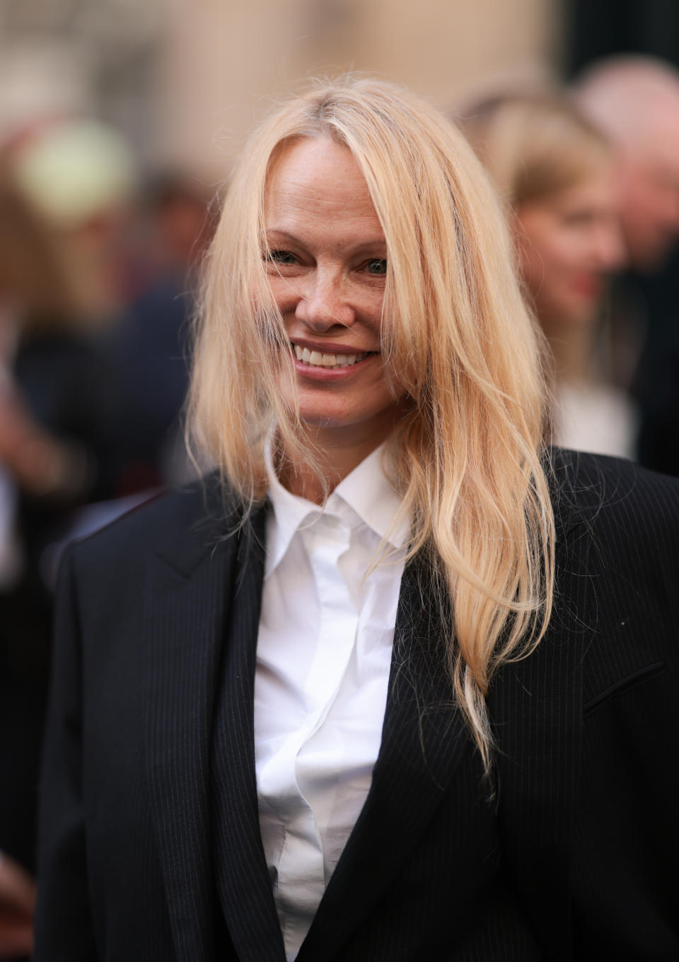 pamela anderson without makeup wearing black suit and white button-down shirt at paris fashion week