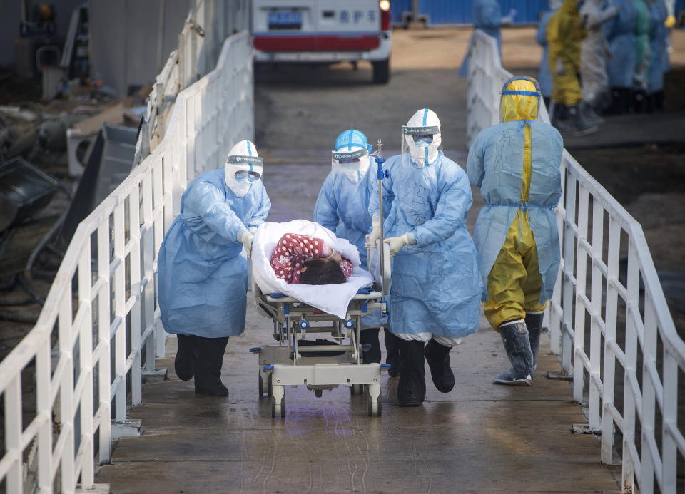 In this photo released by China's Xinhua News Agency, medical workers in protective suits help transfer the first group of patients into the newly-completed Huoshenshan temporary field hospital in Wuhan in central China's Hubei province. China said Tuesday the number of infections from a new virus surpassed 20,000 as medical workers and patients arrived at a new hospital and President Xi Jinping said "we have launched a people's war of prevention of the epidemic." (Xiao Yijiu/Xinhua via AP)