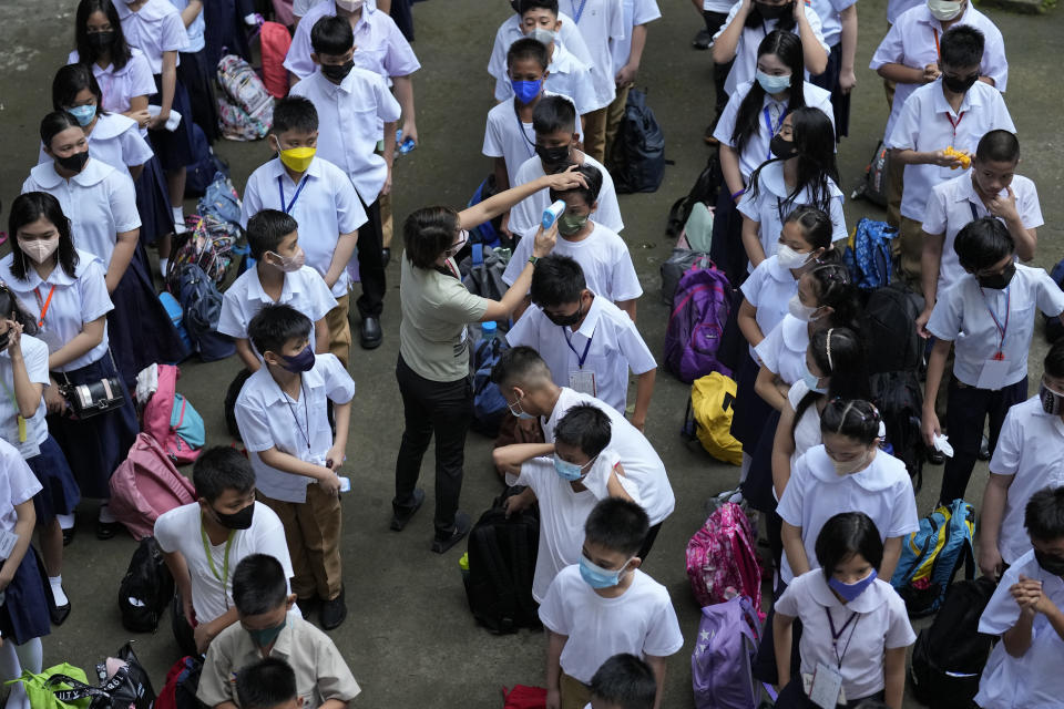 A teacher conducts temperature checks on students during the opening of classes at the San Juan Elementary School in metro Manila, Philippines on Monday, Aug. 22, 2022. Millions of students wearing face masks streamed back to grade and high schools across the Philippines Monday in their first in-person classes after two years of coronavirus lockdowns that are feared to have worsened one of the world's most alarming illiteracy rates among children. (AP Photo/Aaron Favila)