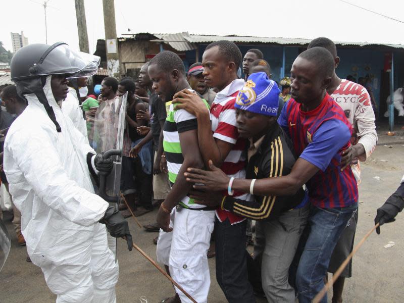 In der liberianischen Hauptstadt Monrovia kontrollieren Polizisten in Schutzanzügen die Ausgabe von Essen an Anwohner. Foto: Foto: Ahmed Jallanzo