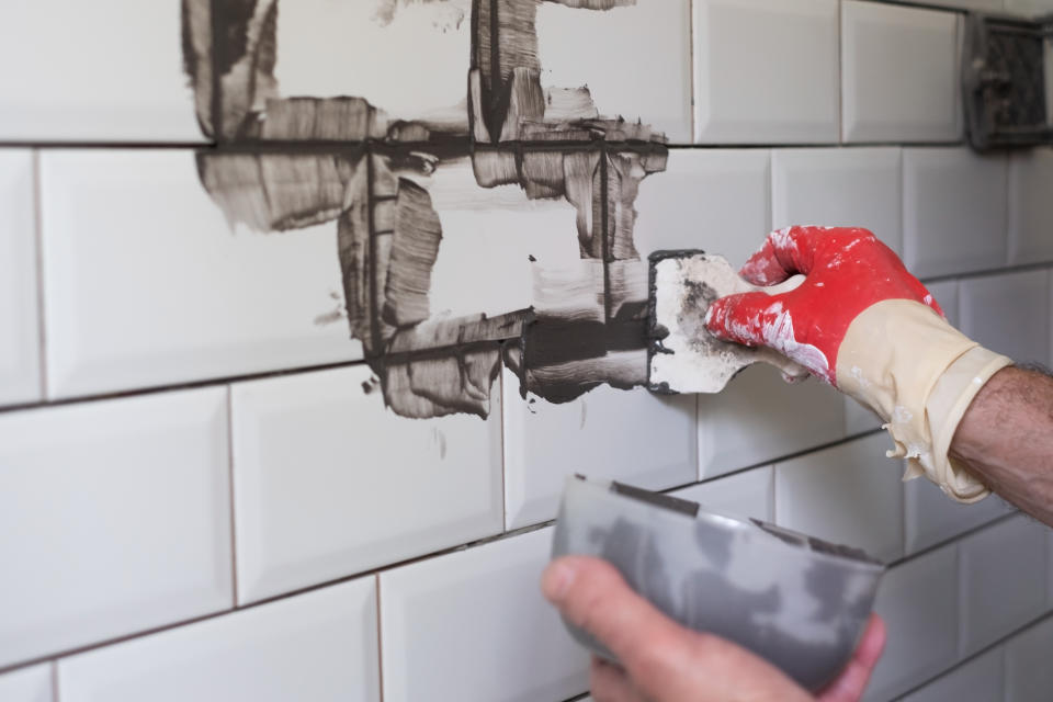 Worker applies grey grout at white tiles with rubber trowel. Kitchen renovation.