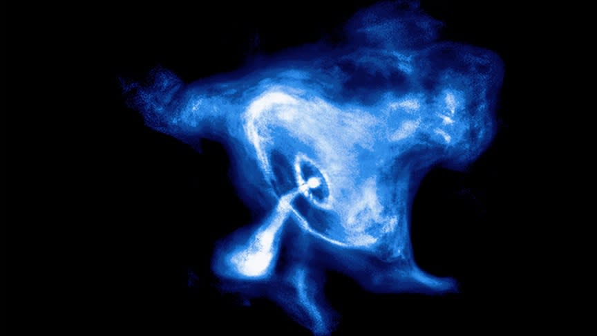  A blue and white glowing view of the Crab Nebula. It looks like there's a ring of gassy material around a dot that's giving off a stream of gas itself. 