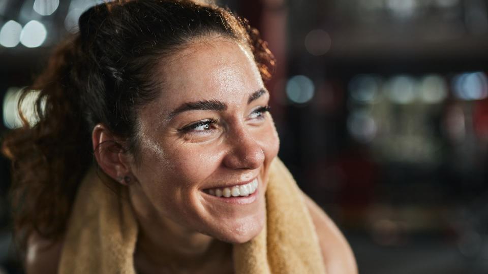 Woman happy with sweaty face and towel around her shoulders at the gym