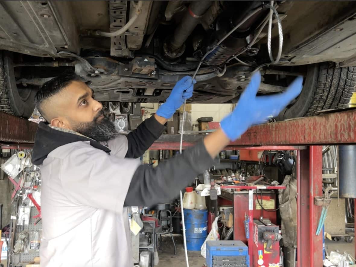 Ravi Chandra, one of the owners of a Minute Muffler shop in northeast Calgary, installs a cable through and around a catalytic converter. (Bryan Labby/CBC - image credit)