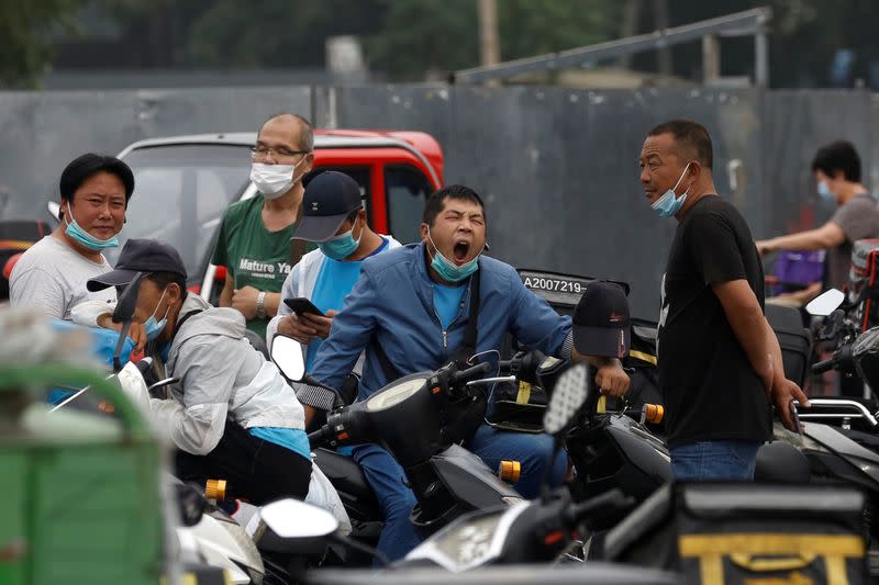 Delivery workers wearing face masks wait for online orders near a street, following the outbreak of the coronavirus disease (COVID-19), in Beijing