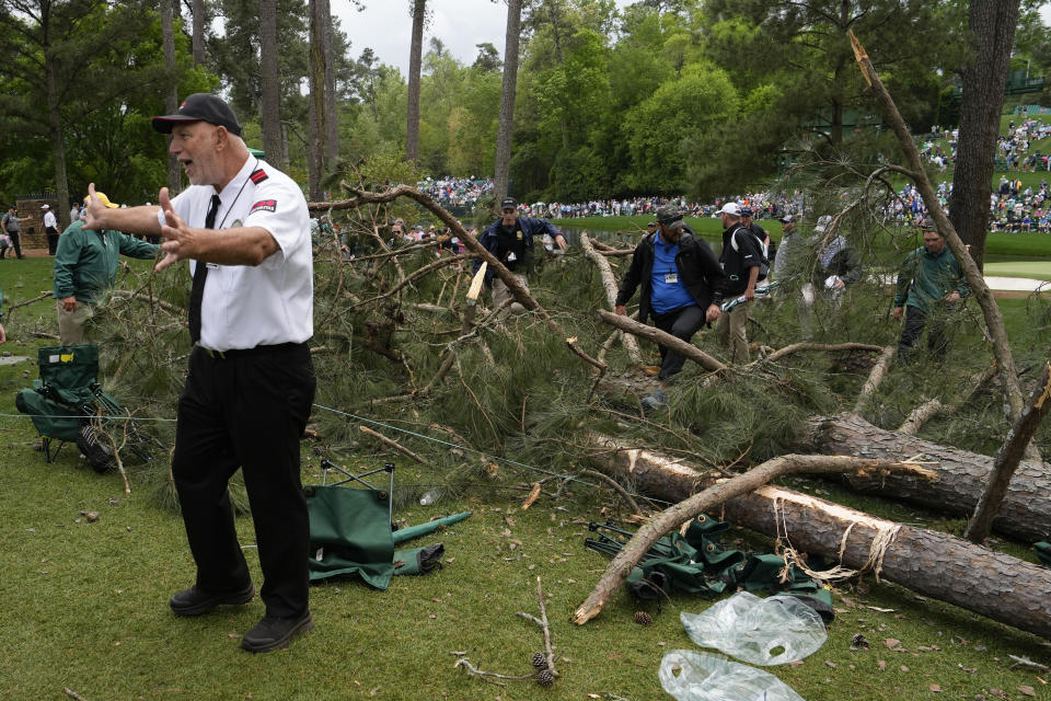 A security guard moves patrons away from trees that blew over on the 17th hole during the second round of the Masters golf tournament at Augusta National Golf Club on Friday, April 7, 2023, in Augusta, Ga. (AP Photo/Mark Baker)