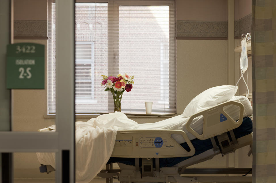 Hospital room with an empty bed, a vase of flowers on the window ledge, and an IV pole beside the bed. Room number 3422