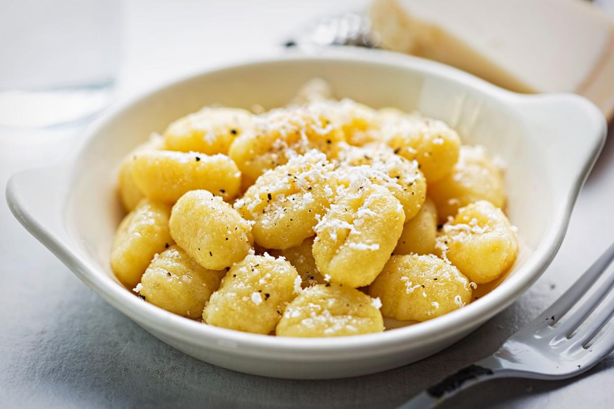 Potato gnocchi with parmesan and olive oil in a white serving bowl with a fork with a blurred background