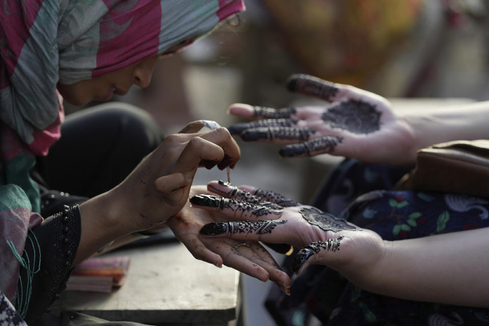 A beautician paints hands of customers with traditional henna in preparation for the upcoming Eid al-Fitr celebrations, in Karachi, Pakistan, Thursday, April 20, 2023. Eid al-Fitr marks the end of the Islamic holy month of Ramadan. (AP Photo/Fareed Khan)