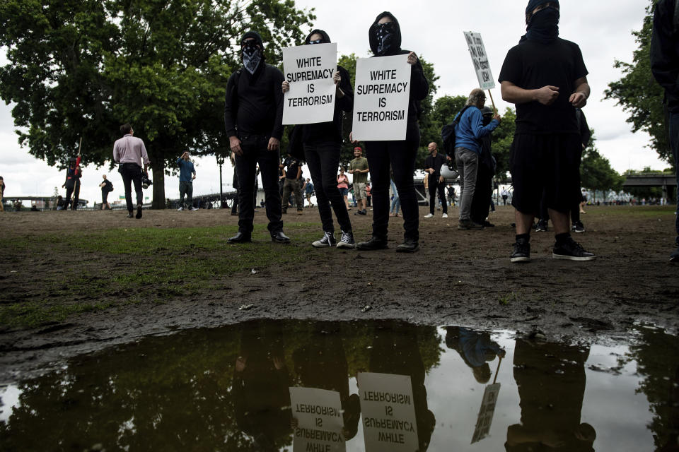 Black-clad protesters, gathered to oppose conservative groups staging an "End Domestic Terrorism" rally, hold signs in Portland, Ore., on Saturday, Aug. 17, 2019. Police have mobilized to prevent clashes between conservative groups and counter-protesters who plan to converge in the city. (AP Photo/Noah Berger)