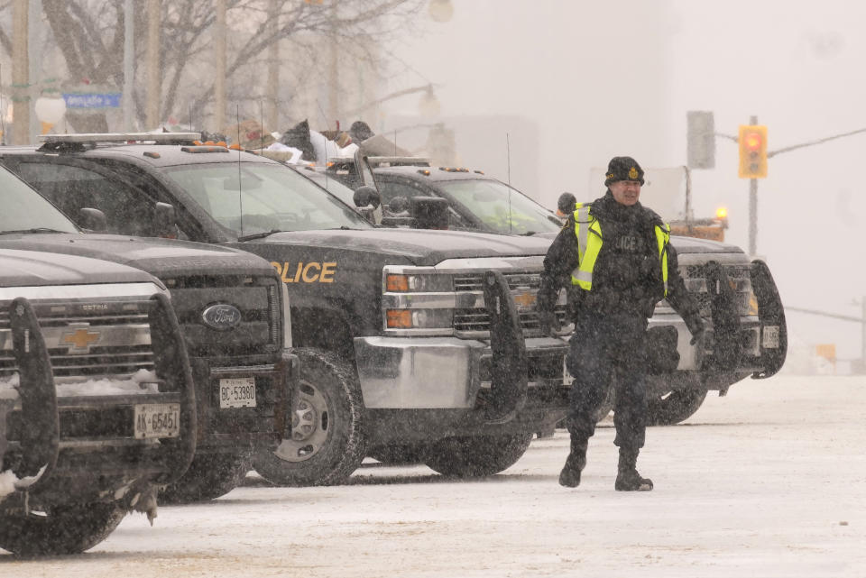 An officer stands next to police vehicles are parked downtown Ottawa on Sunday, Feb. 20, 2022. A protest, which was first aimed at a COVID-19 vaccine mandate for cross-border truckers but also encompassed fury over the range of COVID-19 restrictions. (Adrian Wyld/The Canadian Press via AP)