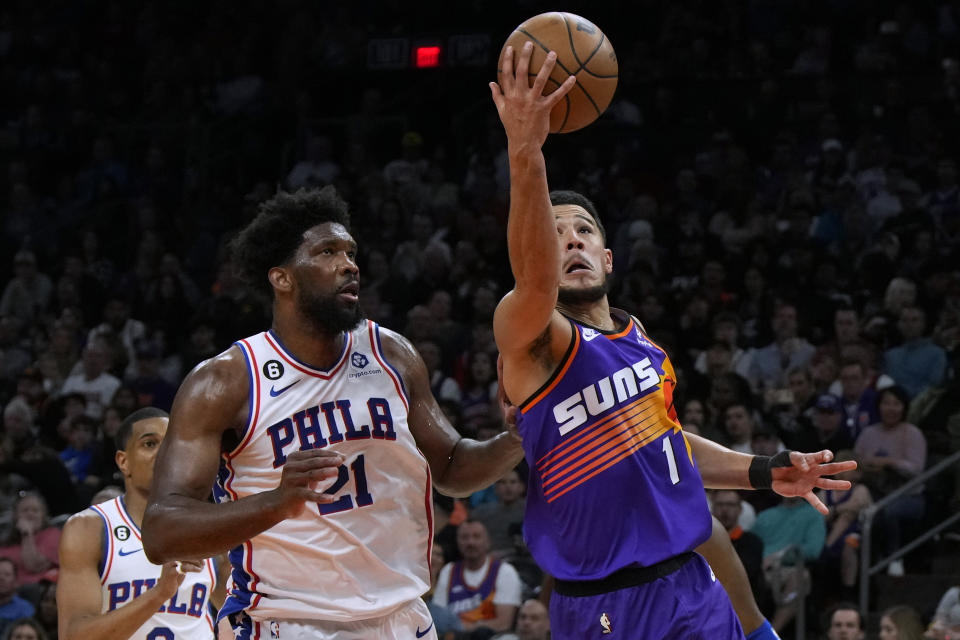 Phoenix Suns guard Devin Booker (1) shoots next to Philadelphia 76ers center Joel Embiid (21) during the second half of an NBA basketball game Saturday, March 25, 2023, in Phoenix. The Suns won 125-105. (AP Photo/Rick Scuteri)