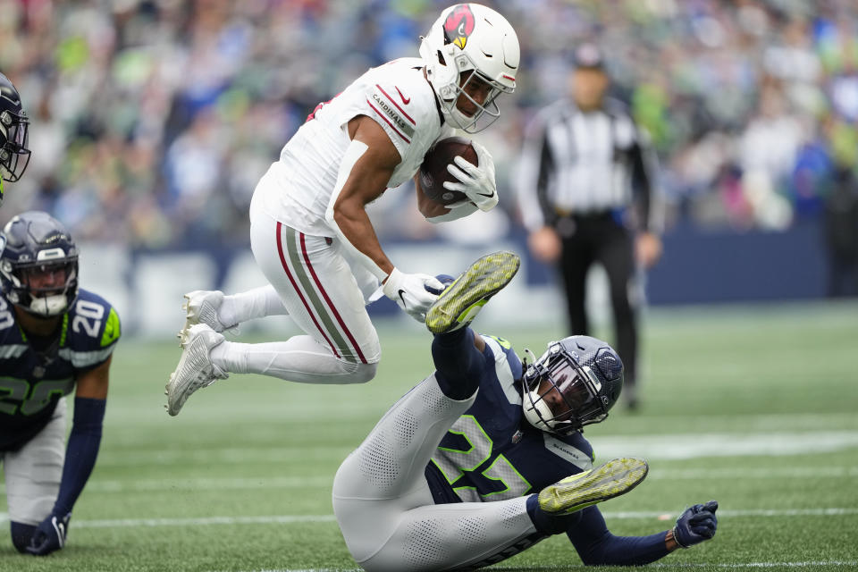 Arizona Cardinals wide receiver Rondale Moore, center, leaps over Seattle Seahawks cornerback Riq Woolen, right, as Seahawks safety Julian Love (20) looks on during the first half of an NFL football game Sunday, Oct. 22, 2023, in Seattle. (AP Photo/Lindsey Wasson)