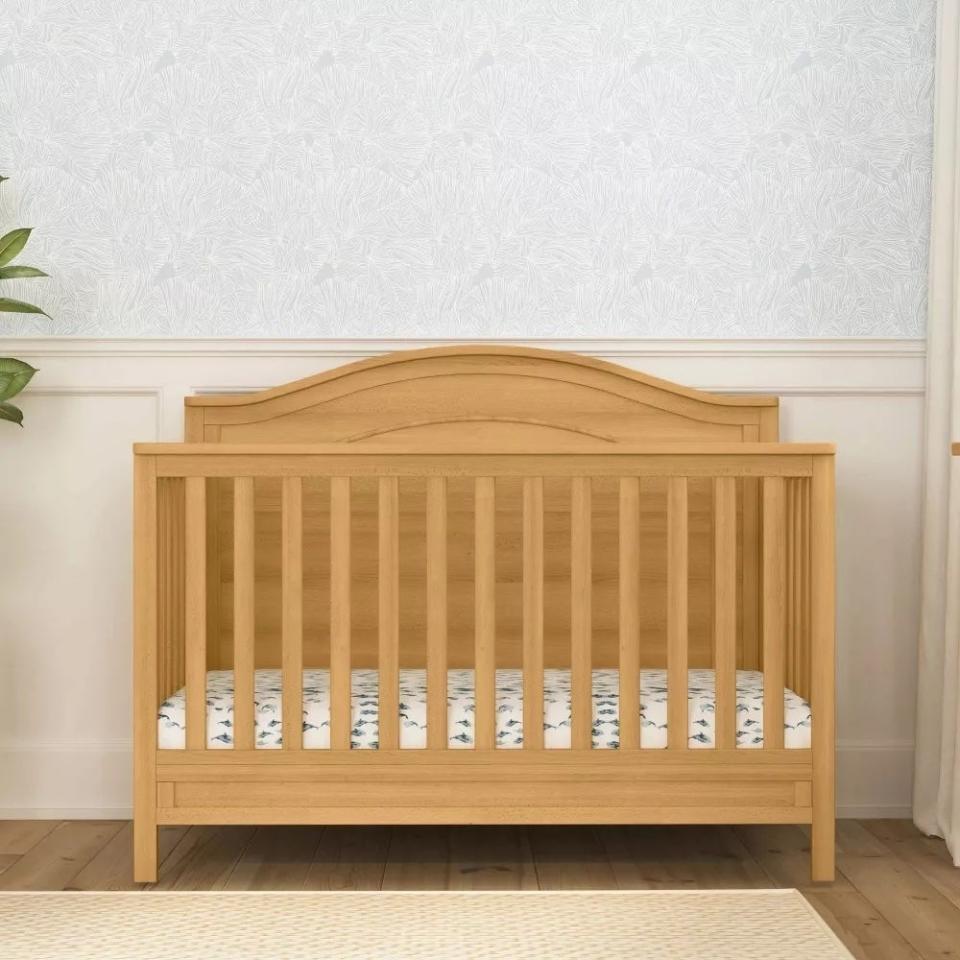 Wooden crib against a patterned wall, no bedding, for a shopping article on nursery furniture