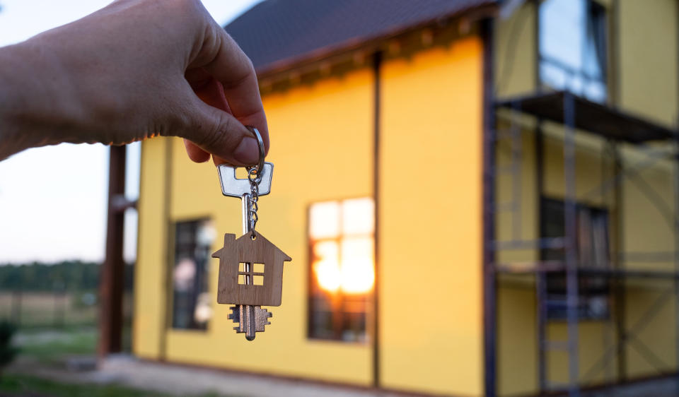 A hand with the keys to a new house on the background of an unfinished cottage. Building, project, moving to a new home, mortgage, rent and purchase real estate. To open the door. Copy space