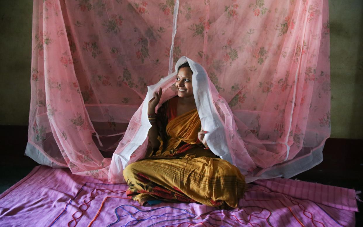 Utkalika Swain, 21, sits under the mosquito net that her and her sisters sleep under in Chhanghar village, Odisha - Catherine Davison