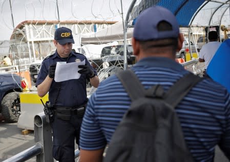 A U.S. Customs and Border Protection officer inspects documents from a Honduran migrant seeking asylum at Paso del Norte International border bridge, in this picture taken from Ciudad Juarez