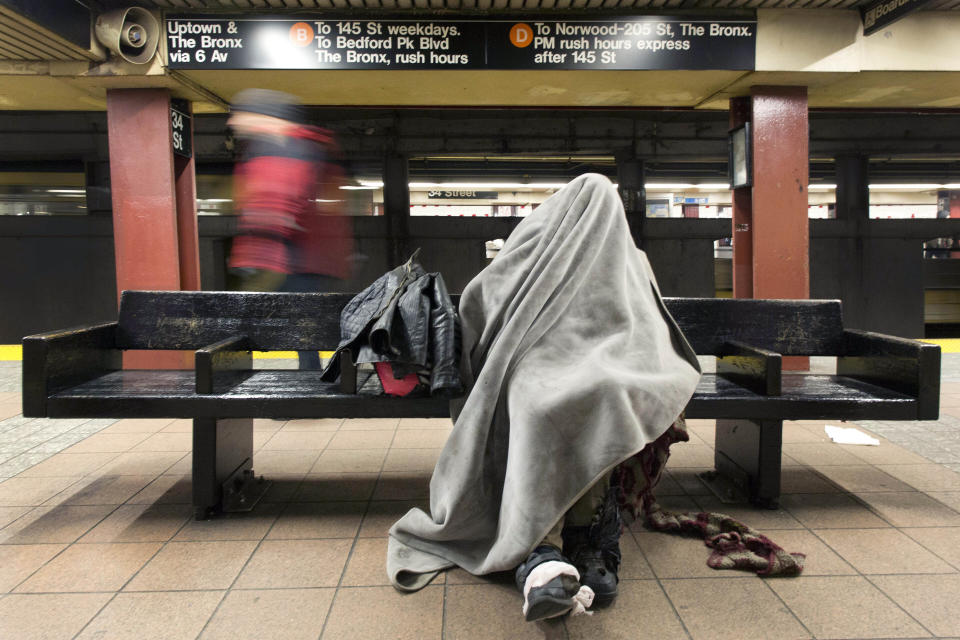 FILE - A man sits under a blanket on a bench in a New York subway station, on Jan. 28, 2014. New York Mayor Eric Adams is announcing a plan to boost safety in the city's sprawling subway network and try to stop homeless people from sleeping on trains or living in stations. (AP Photo/Mark Lennihan, File)