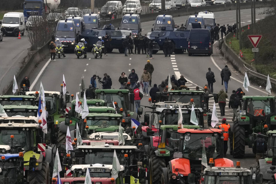 Tractores colocados ante vehículos de las fuerzas de seguridad en una autopista cortada, el miércoles 31 de enero de 2024 en Chilly-Mazarin, en el sur de París. Grupos de agricultores bloquearon más carreteras en Bélgica, Francia e Italia el miércoles, en un intento de complicar la actividad de grandes puertos y núcleos económicos. También se acercaban a Bruselas la víspera de una importante cumbre de la Unión Europea, en un esfuerzo de conseguir mejores precios por sus productos y menos burocracia para hacer su trabajo. (AP Foto/Thibault Camus)