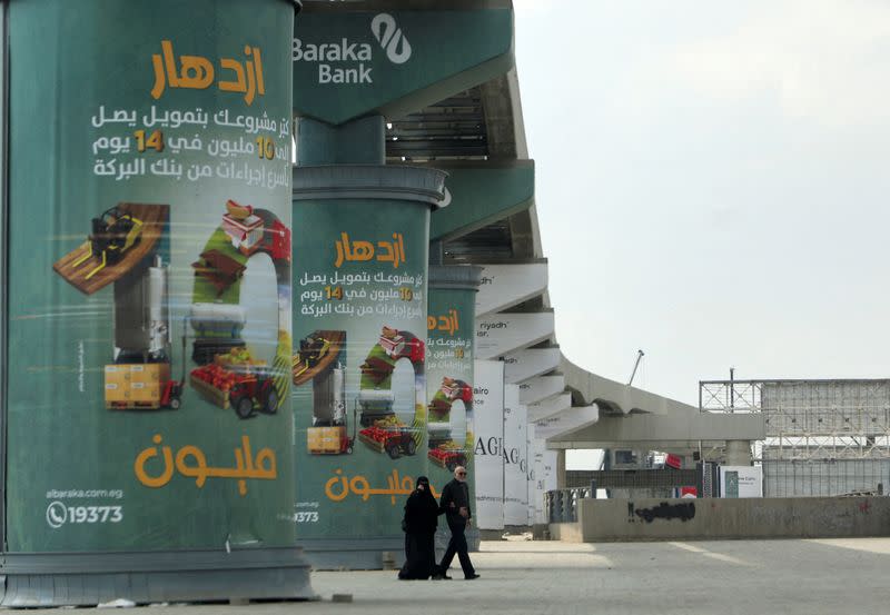 FILE PHOTO: An Egyptian couple walks next to advertising credit investment certificates by branch of Al Baraka Bank in Cairo