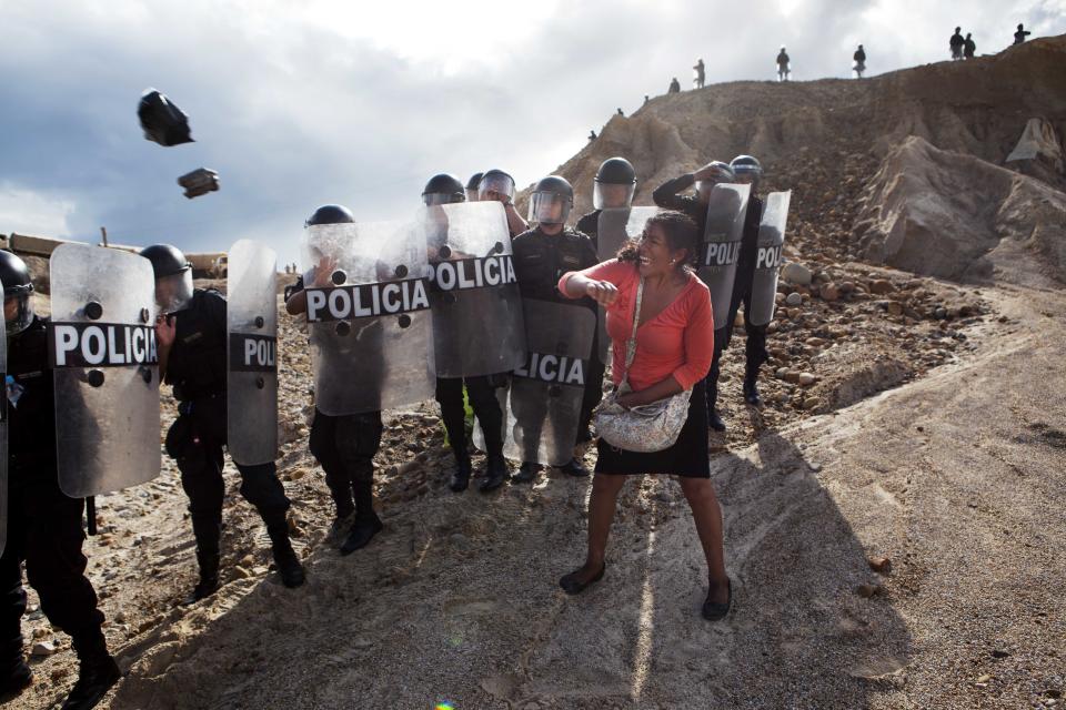 A woman throws a rock and a bag at riot policemen who block her way home in Huepetuhe district in Peru's Madre de Dios region in Peru, Monday, April 28, 2014. Soldiers, police and marines have begun destroying illegal gold mining machinery in Peru’s southeastern jungle region of Madre de Dios. Authorities began enforcing a ban on illegal mining Monday in the Huepetuhe district. Before the deadline, miners clashed with police while intermittently blocking traffic on the Interoceanic Highway that links the Pacific with Brazil. (AP Photo/Rodrigo Abd)