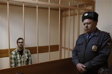 Videographer Kieron Bryan of Britain, one of the 30 people who were arrested over a Greenpeace protest at the Prirazlomnaya oil rig, looks out from a defendants' cage as he attends a court session in St. Petersburg, November 18, 2013. REUTERS/Alexander Demianchuk