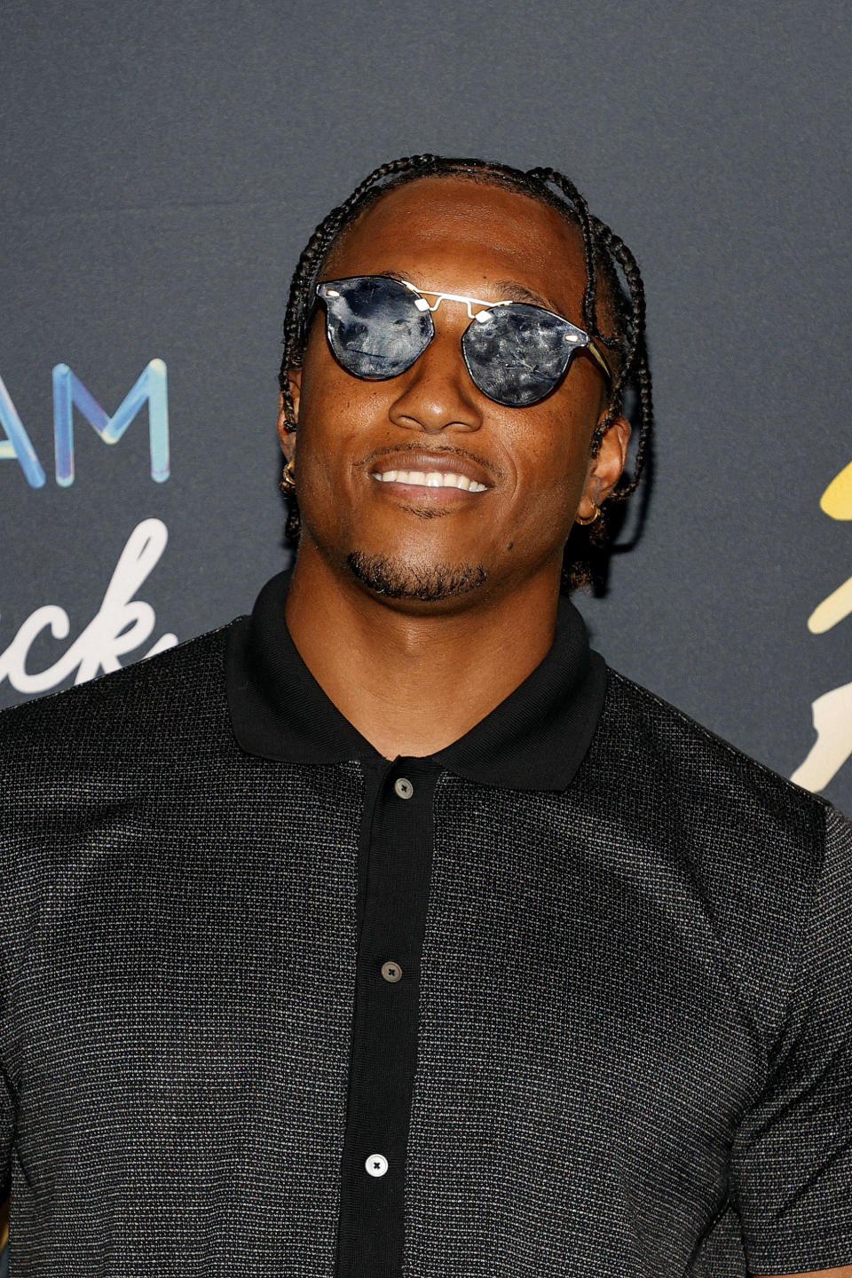 A close-up of smiling Lecrae at a red carpet event and wearing sunglasses