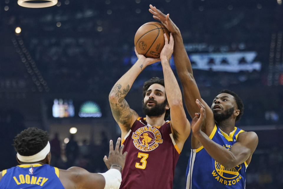 Golden State Warriors' Andrew Wiggins (22) knocks the ball loose from Cleveland Cavaliers' Ricky Rubio (3) as Kevon Looney (5) watches in the first half of an NBA basketball game, Thursday, Nov. 18, 2021, in Cleveland. (AP Photo/Tony Dejak)