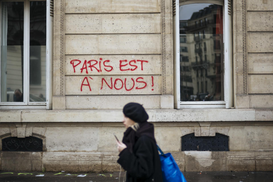 A woman walks past graffiti reading "Paris is ours", near the Arc de Triomphe, in Paris, Sunday, Dec. 2, 2018. A protest against rising taxes and the high cost of living turned into a riot in the French capital Saturday, as activists caused widespread damage and tagged the Arc de Triomphe with multi-colored graffiti during clashes with police. (AP Photo/Kamil Zihnioglu)