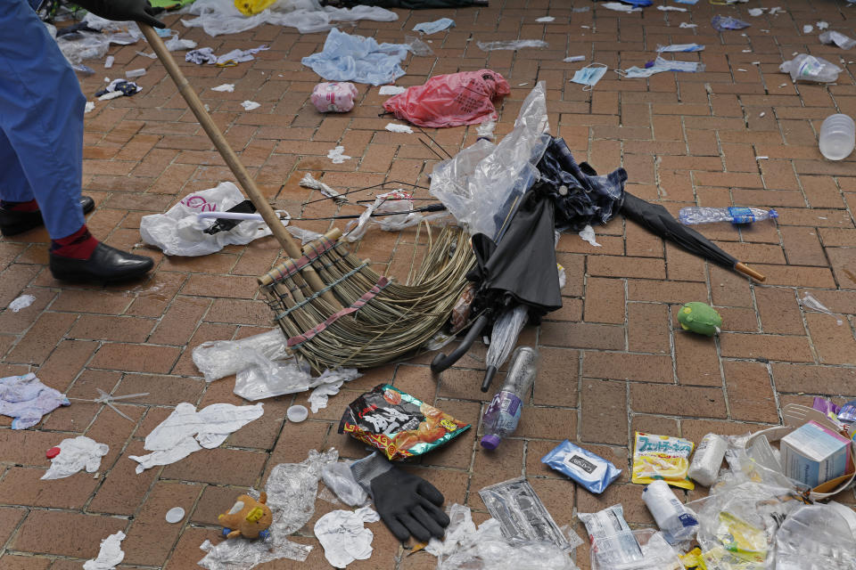 In this Friday, June 14, 2019, photo, a worker cleans up broken umbrellas left in the aftermath of Wednesday's violent protest against proposed amendments to an extradition law in Hong Kong. Umbrellas became a symbol of protest in Hong Kong in 2014 after demonstrators used them to shield themselves from both police pepper spray and a hot sun. Five years later, umbrellas were out in force again on Wednesday as thousands of protesters faced off with police outside the legislature. (AP Photo/Vincent Yu)