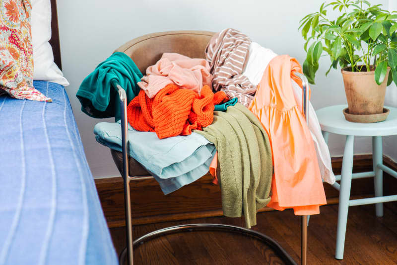 A pile of laundry on a chair between a bed and a small table with potted plant