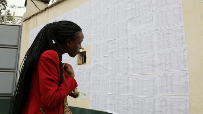 A woman wearing red with long braids looking for her name against an extensive list.