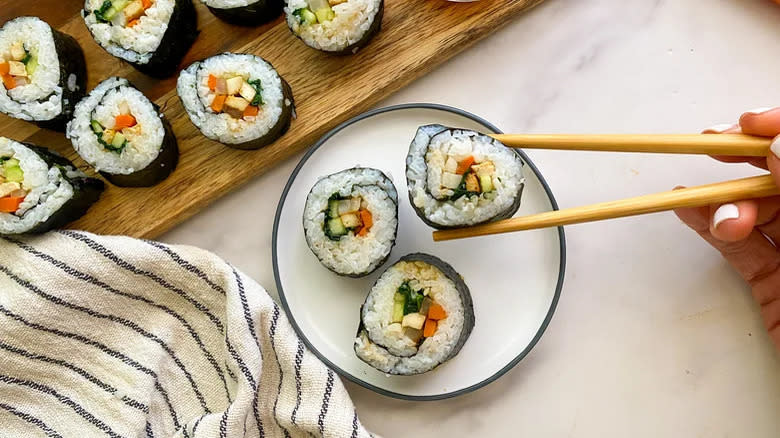 Top-down view of plated vegetarian kimbap sushi with  one piece held in chopsticks